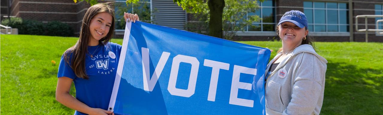 Two students holding up a blue flag that says "vote"